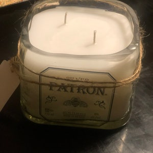 May include: A clear glass candle jar with a white candle and two wicks. The jar is wrapped with twine and has a label that reads "GILLED PATRON" with a bee logo and the text "HECHO EN MEXICO MADE IN MEXICO 750 ml 40% ntc/val".