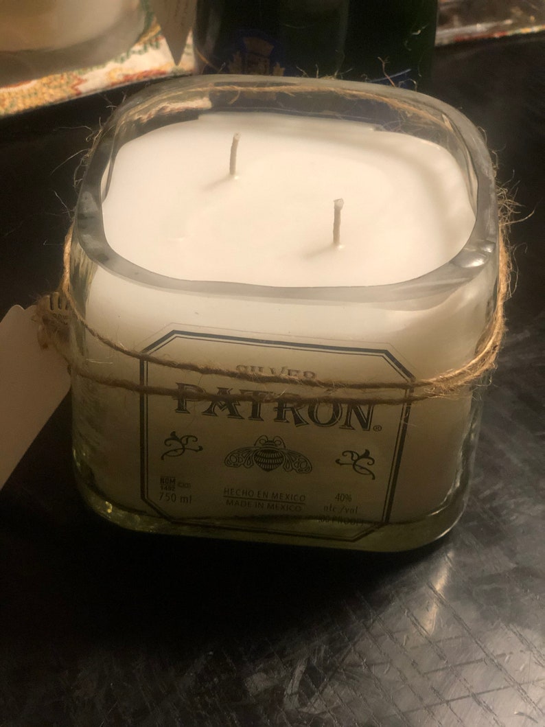 May include: A clear glass candle jar with a white candle and two wicks. The jar is wrapped with twine and has a label that reads "GILLED PATRON" with a bee logo and the text "HECHO EN MEXICO MADE IN MEXICO 750 ml 40% ntc/val".