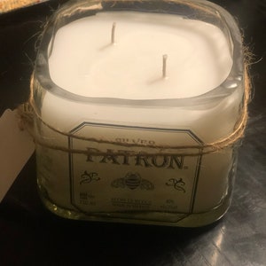May include: A clear glass candle jar with a white candle and two wicks. The jar is wrapped with twine and has a label that reads "PATRON. SILVERO HECHO EN MEXICO MADE IN MEXICO 750 ml 40% alc/vol."