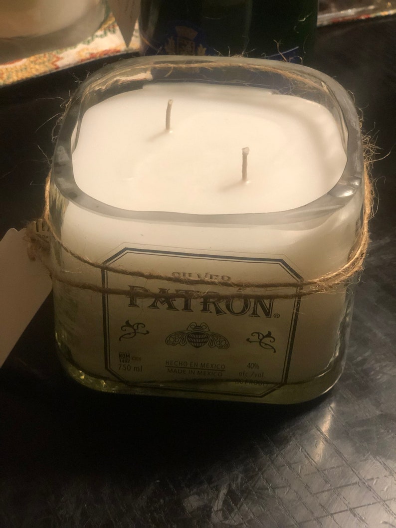 May include: A clear glass candle jar with a white candle and two wicks. The jar is wrapped with twine and has a label that reads "PATRON. SILVERO HECHO EN MEXICO MADE IN MEXICO 750 ml 40% alc/vol."
