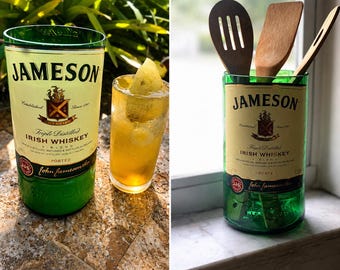 May include: A green glass container repurposed from a Jameson Irish Whiskey bottle, featuring the original cream-colored label with black text and a red crest. The container holds three wooden kitchen utensils, including a slotted spoon and spatula.