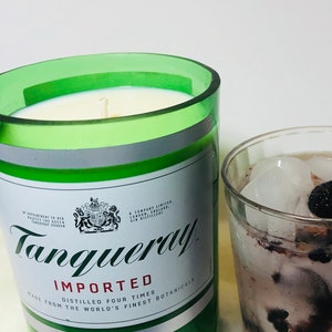 K&ouml;nnte beinhalten: Eine gr&uuml;ne Glaskerze in Form einer Tanqueray Gin-Flasche. Die Kerze hat ein wei&szlig;es Etikett mit dem Tanqueray-Logo und dem Text "Importiert, Vierfach Destilliert, Hergestellt aus den feinsten Botanicals der Welt, London Dry Gin, Abgef&uuml;llt in Gro&szlig;britannien f&uuml;r Charles Tanqueray & Co., 47,3% Alc. Vol. (94,6 Proof)".