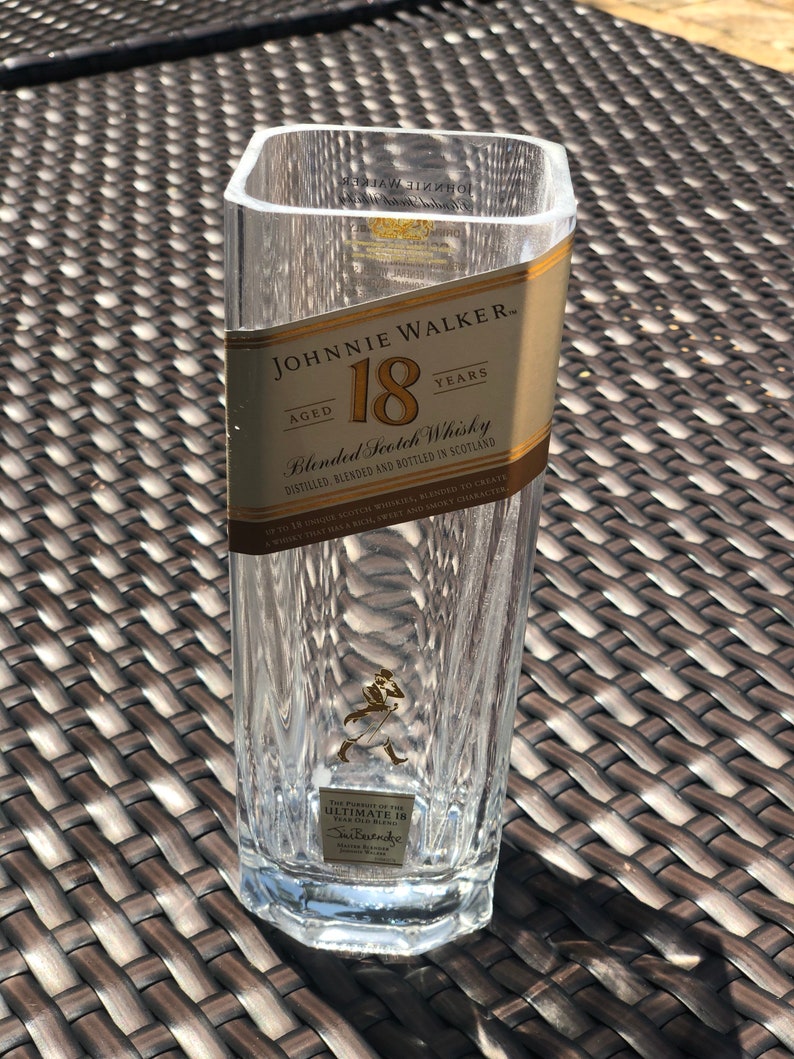 May include: A clear glass bottle with a gold label that reads "JOHNNIE WALKER AGED 18 YEARS Blended Scotch Whisky". The bottle is sitting on a brown wicker surface.