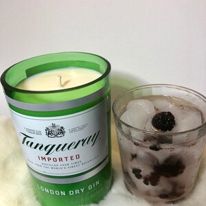K&ouml;nnte beinhalten: Ein gr&uuml;nes Glas-Kerzengef&auml;&szlig; mit einer wei&szlig;en Kerze darin. Das Gef&auml;&szlig; ist mit "Tanqueray Imported London Dry Gin" beschriftet. Im Hintergrund ein Glas mit Eis und Brombeeren.