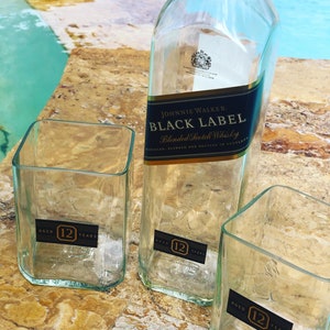 Op de afbeelding: Drie lege glazen flessen, twee zijn vierkant en &eacute;&eacute;n is hoog en rechthoekig. De flessen zijn gelabeld met "Johnnie Walker Black Label Blended Scotch Whisky" en "12 jaar oud".