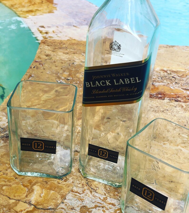 Op de afbeelding: Drie lege glazen flessen, twee zijn vierkant en &eacute;&eacute;n is hoog en rechthoekig. De flessen zijn gelabeld met "Johnnie Walker Black Label Blended Scotch Whisky" en "12 jaar oud".