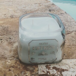 May include: A clear glass candle jar with a white candle inside. The jar is labeled "SILVER PATR&Oacute;N" with the text "HECHO EN MEXICO" and "750 ml".