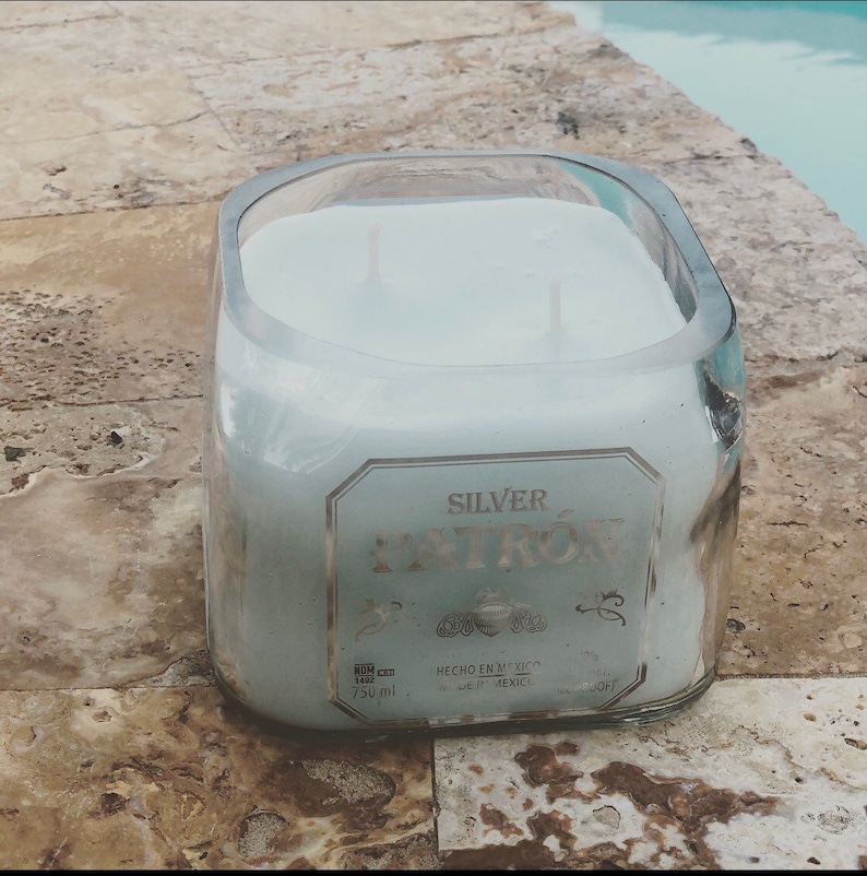May include: A clear glass candle jar with a white candle inside. The jar is labeled "SILVER PATR&Oacute;N" with the text "HECHO EN MEXICO" and "750 ml".