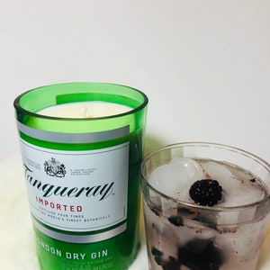 K&ouml;nnte beinhalten: Ein gr&uuml;nes Glas-Kerzengef&auml;&szlig; mit einem wei&szlig;en Etikett, auf dem "Tanqueray Imported" und "London Dry Gin" steht. Das Kerzengef&auml;&szlig; steht auf einer wei&szlig;en Oberfl&auml;che neben einem Glas mit Eis und Brombeeren.