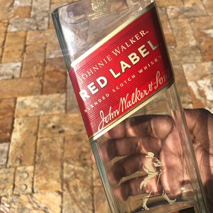 May include: Empty glass bottle with a red label that says "Johnnie Walker Red Label Blended Scotch Whisky" and a gold label that says "John Walker & Sons Established".