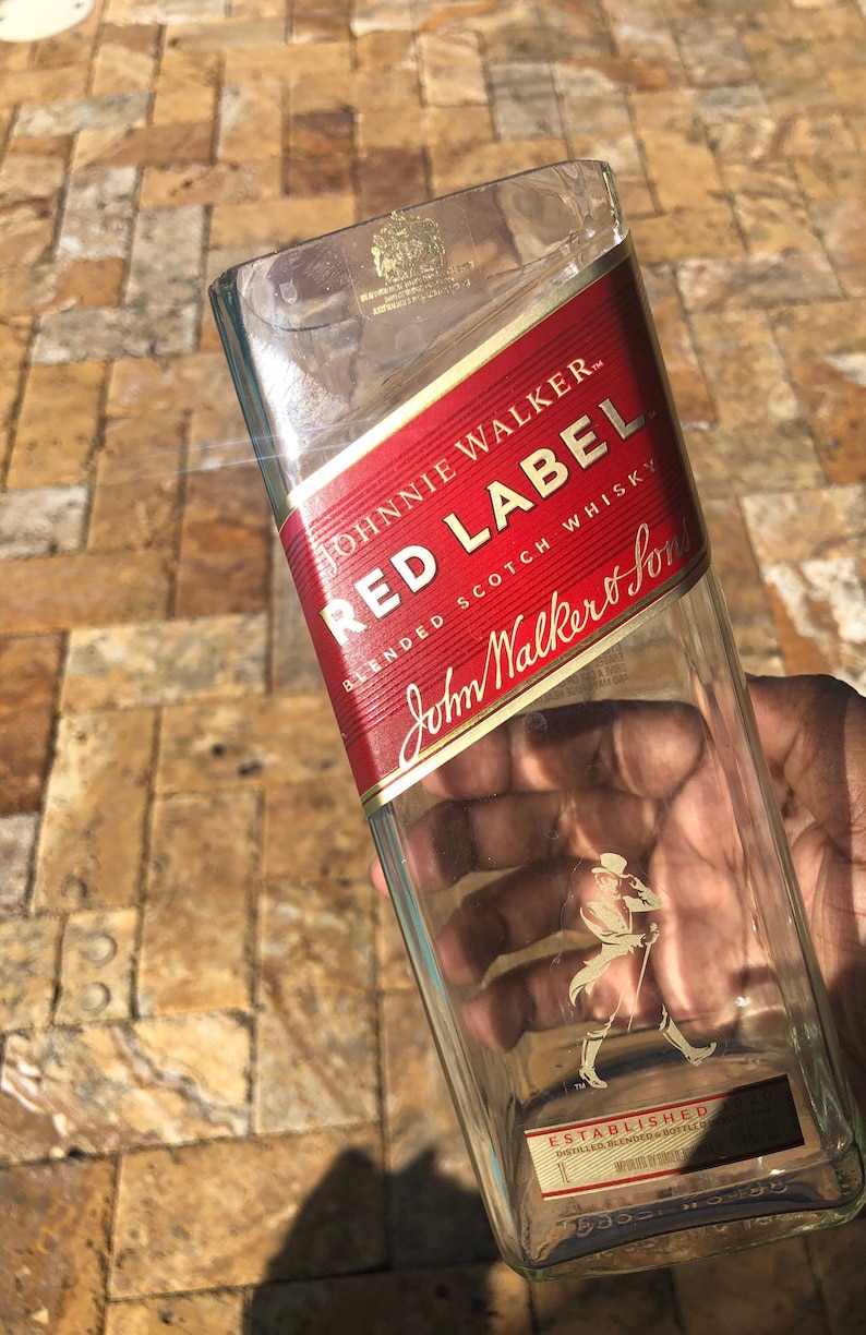May include: Empty glass bottle with a red label that says "Johnnie Walker Red Label Blended Scotch Whisky" and a gold label that says "John Walker & Sons Established".