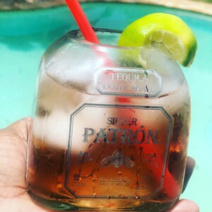 May include: A glass bottle filled with a clear liquid and ice cubes. The bottle is labeled "Tequila 100% de Agave" and "Silver Patron". A lime wedge and a red straw are in the bottle.