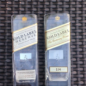 May include: Two clear glass bottles of Johnnie Walker Gold Label Reserve Blended Scotch Whisky. The bottle on the left is labeled "Gold Label Reserve" and the bottle on the right is labeled "Gold Label The Centenary Blend". The bottle on the right is aged 18 years.