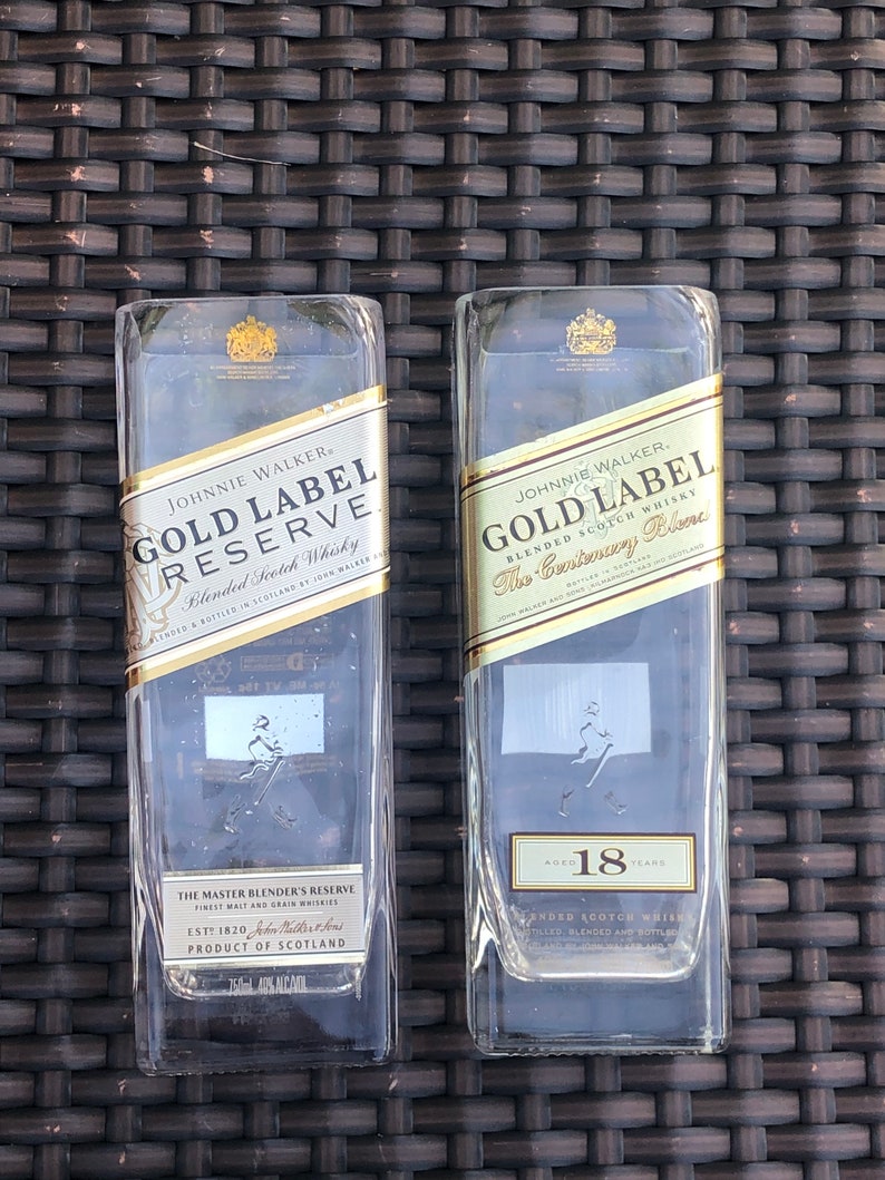 May include: Two clear glass bottles of Johnnie Walker Gold Label Reserve Blended Scotch Whisky. The bottle on the left is labeled "Gold Label Reserve" and the bottle on the right is labeled "Gold Label The Centenary Blend". The bottle on the right is aged 18 years.