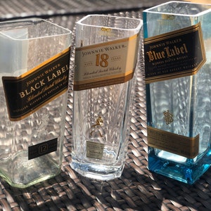 May include: Three empty glass bottles with Johnnie Walker labels. The bottles are labeled Black Label, 18 Years, and Blue Label. The bottles are sitting on a brown wicker surface.