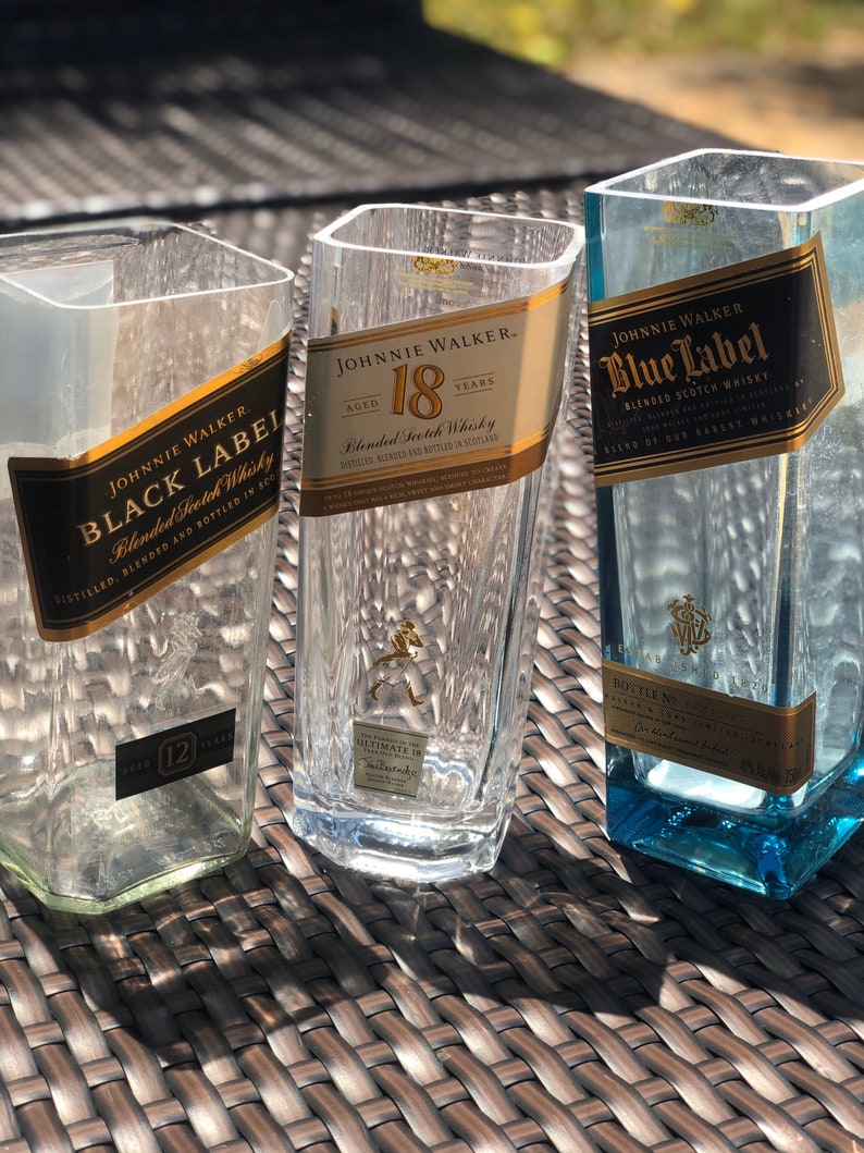 May include: Three empty glass bottles with Johnnie Walker labels. The bottles are labeled Black Label, 18 Years, and Blue Label. The bottles are sitting on a brown wicker surface.