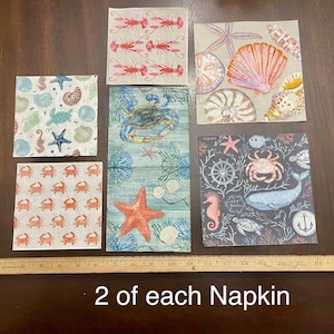 May include: Set of 10 fabric napkins with nautical themes. The designs include a crab, starfish, seashells, a whale, a seahorse, and a sailboat. The napkins are white with colorful designs.