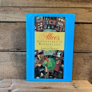 May include: A blue hardcover book with the title "Alice's Adventures in Wonderland" by Lewis Carroll, illustrated by Anthony Browne. The cover features an illustration of Alice falling down a rabbit hole.