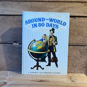 May include: A vintage book cover with a blue and white striped background. The title is "Around the World in 80 Days" in a bold, white font. The cover features an illustration of two men standing next to a globe. The text "A Golden Illustrated Classic" is at the bottom of the cover.