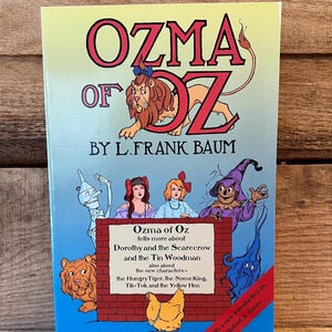 May include: A vintage copy of "Ozma of Oz" by L. Frank Baum. The book cover features the title in large red letters with a lion illustration. The cover also includes illustrations of Dorothy, the Scarecrow, the Tin Woodman, and other characters.