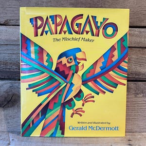 May include: A children's book titled "PAPAGAYO The Mischief Maker" with a vibrant illustration of a colorful parrot on a yellow background. The book cover also includes the author's name, Gerald McDermott.