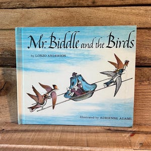 May include: A vintage children's book titled "Mr. Biddle and the Birds" by Lonzo Anderson, illustrated by Adrienne Adams. The cover features a light blue sky with illustrations of birds and a character in a blue carriage.