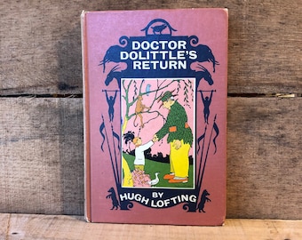 Puede incluir: Un libro antiguo de tapa dura titulado "El regreso del doctor Dolittle" de Hugh Lofting. La portada presenta una ilustración colorida del doctor Dolittle y un niño pequeño dándose la mano, rodeados de animales y un cielo rosa.