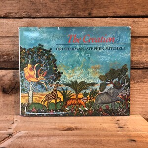 May include: A vintage children's book titled "The Creation" by Ori Sherman and Stephen Mitchell. The cover features a colorful illustration of a giraffe, tiger, elephant, and a woman with wings in a lush, tropical setting.