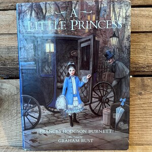 May include: A Little Princess book cover featuring a young girl in a blue coat standing near a carriage. The cover includes the title, author, and illustrator's names. The illustration has a vintage style with a dark, atmospheric background.
