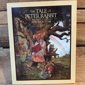 May include: A hardcover book titled The Tale of Peter Rabbit and Other Stories by Beatrix Potter, illustrated by Allen Atkinson. The cover features a colorful illustration of anthropomorphic rabbits and a cat under a tree with a rainbow.