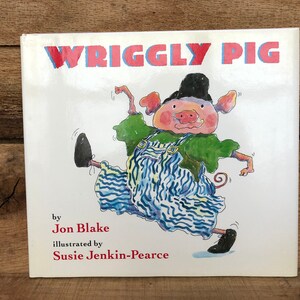 May include: A children's book cover with the title "WRIGGLY PIG" in red and blue letters. The cover features an illustration of a pig wearing a green shirt, blue and white overalls, and a black hat. The pig is dancing with its legs in the air.