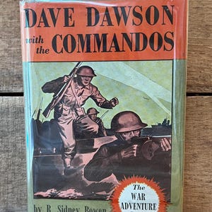May include: A hardcover book titled Dave Dawson with the Commandos by R. Sidney Bowen. The orange and green dust jacket features a vintage illustration of soldiers in helmets with rifles and a machine gun, plus a red burst label for The War Adventure Series.