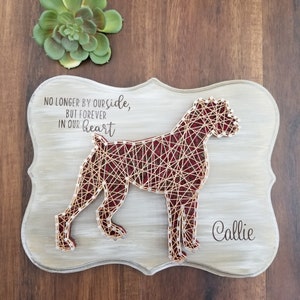 May include: A wooden sign with a decorative border features a string art Boxer dog silhouette. The dog is made with red thread and white nails. The sign includes the text "NO LONGER BY OUR SIDE, BUT FOREVER IN OUR HEART" and the name "Callie".