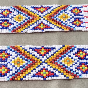 May include: A close-up of a beaded trim with a geometric pattern in shades of red, blue, yellow, white, and brown. The beads are arranged in a repeating pattern of squares and circles.