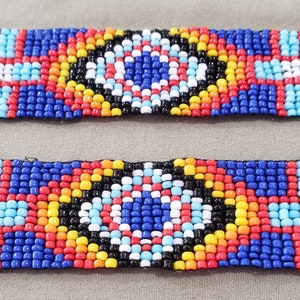 May include: A close-up of a colorful beaded bracelet with a geometric pattern. The bracelet is made of small, round beads in shades of blue, red, yellow, white, and black. The beads are arranged in a repeating pattern of squares and circles.