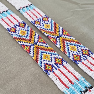 May include: Two beaded strips with a white background and colorful geometric patterns. The patterns include red, blue, yellow, orange, and black beads.