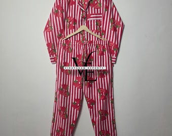 May include: Red and white striped pajama set with a strawberry pattern. The set includes a button-down shirt with a chest pocket and matching pants. The pajamas are hanging on a wooden hanger. The text "VINAYAKAM EXPORTS" is visible.