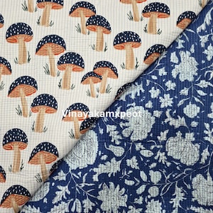 Puede incluir: Dos muestras de tela. Una presenta un patrón repetido de setas con sombreros con puntos azules, branquias naranjas y tallos color canela sobre un fondo crema. La otra tiene un diseño floral azul.