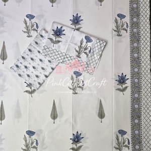 May include: A white fabric featuring a repeating pattern of blue flowers and grey leaf motifs. The border displays a grey lattice design with small blue flowers. The text PinkCityArtCraft is printed in the center of the fabric.