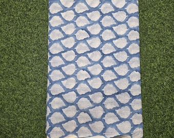 May include: A blue and white patterned fabric with a leaf design, hanging from a wooden hanger. The fabric features a repeating pattern of white leaves on a blue background. The fabric is likely cotton or linen.