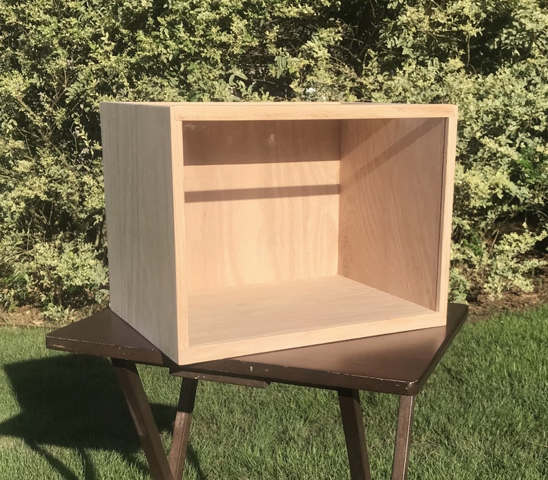 May include: A wooden box with a clear front and a light wood finish. The box is empty and sits on a dark brown table.