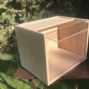 May include: A wooden box with a clear acrylic lid. The box is open and the lid is propped up on the back edge. The box is sitting on a brown wooden table.