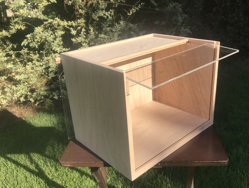 May include: A wooden box with a clear acrylic lid. The box is open and the lid is propped up on the back edge. The box is sitting on a brown wooden table.