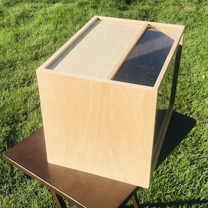 May include: A wooden box with a glass front. The box is light brown and has a simple design.