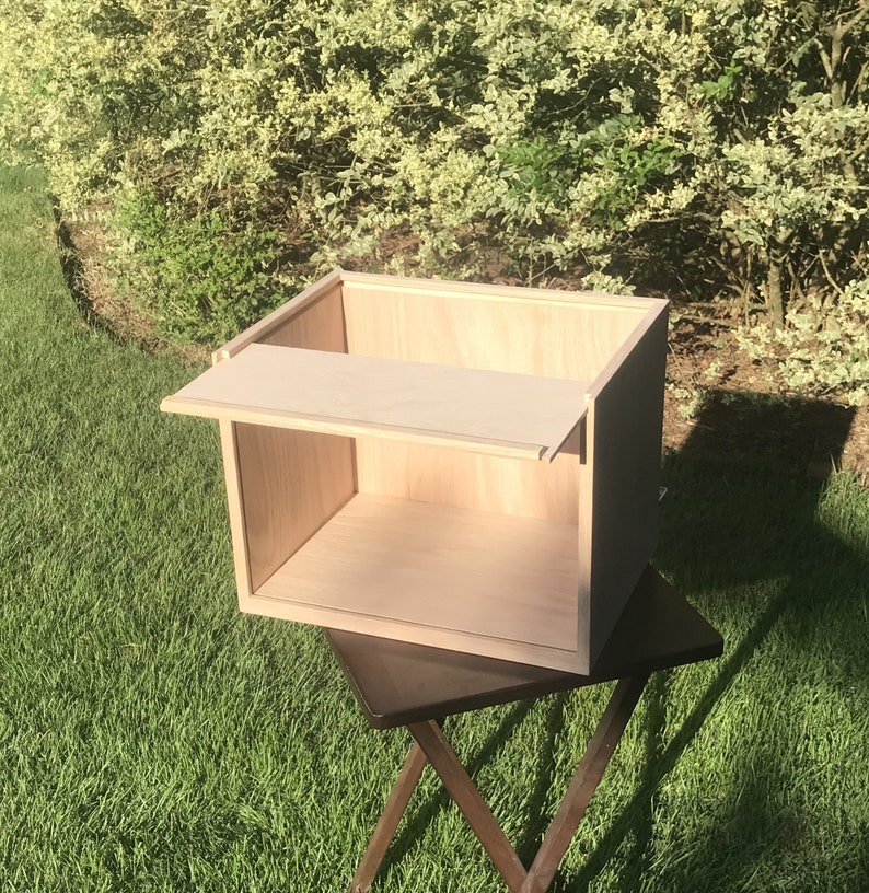 May include: A light wood box with a hinged lid and a shelf inside. The box is sitting on a dark wood table.