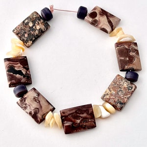 May include: A brown and white patterned stone necklace with purple beads and white shell accents.