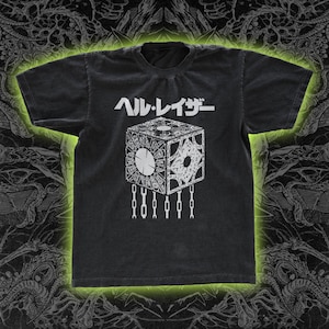 May include: Dark gray t-shirt featuring a white graphic of a puzzle box with chains and Japanese text. The t-shirt has a crew neck and short sleeves. The design is centered on the front of the shirt.