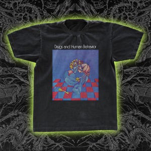May include: Dark gray t-shirt with the text "Drugs and Human Behavior" above a colorful graphic. The graphic features a figure with a spoon on a red and blue checkered floor.