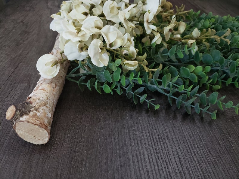 May include: A white and green floral arrangement with white flowers and green leaves on a brown wooden surface.