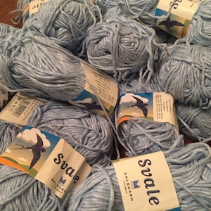 Puede incluir: Un montón de ovillos de lana azul claro con etiquetas que dicen "Svale Dalegarn" y muestran un pájaro en vuelo.